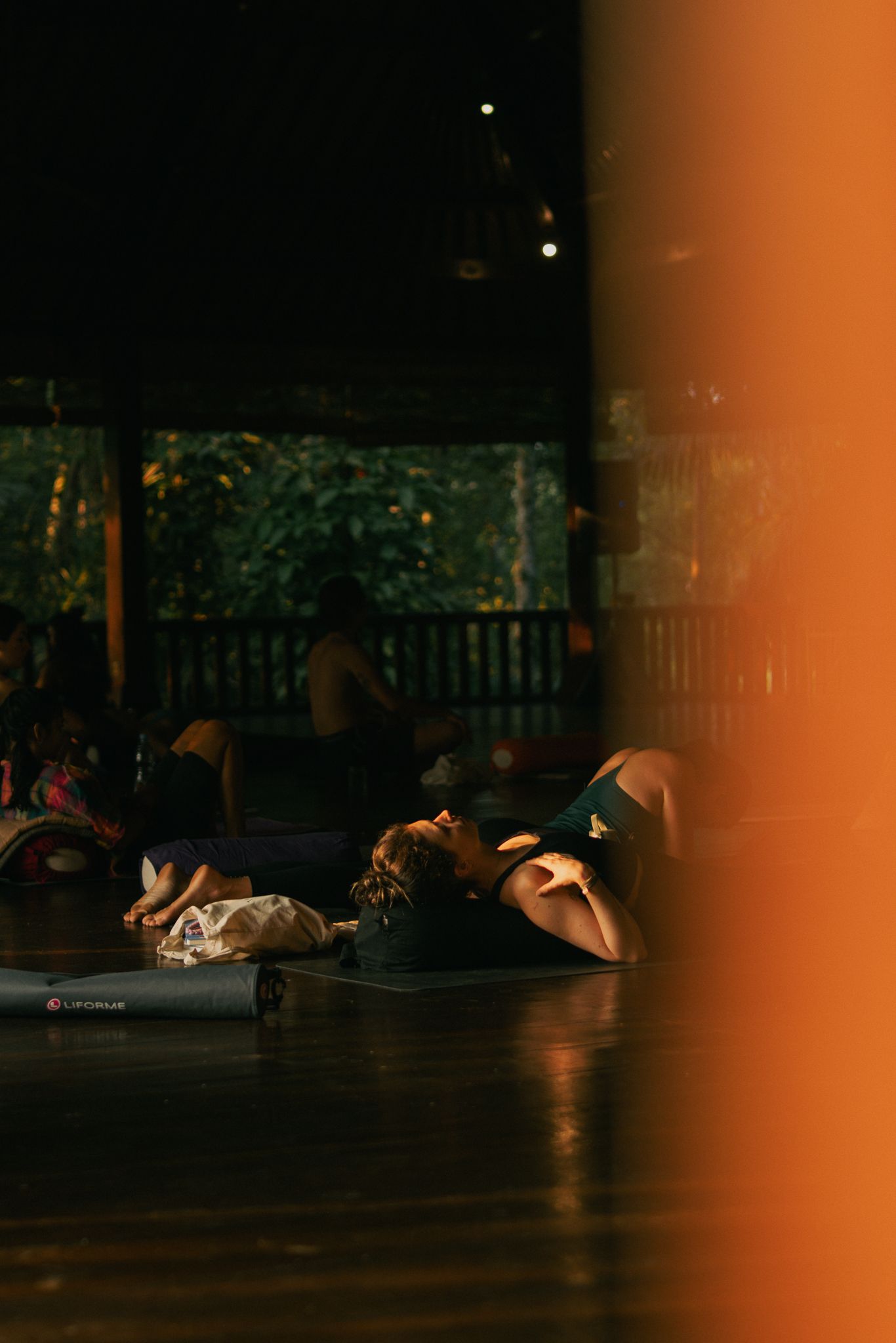 Dancers lying on a dark wooden stage floor during a performance, with warm lighting and railing in the background.