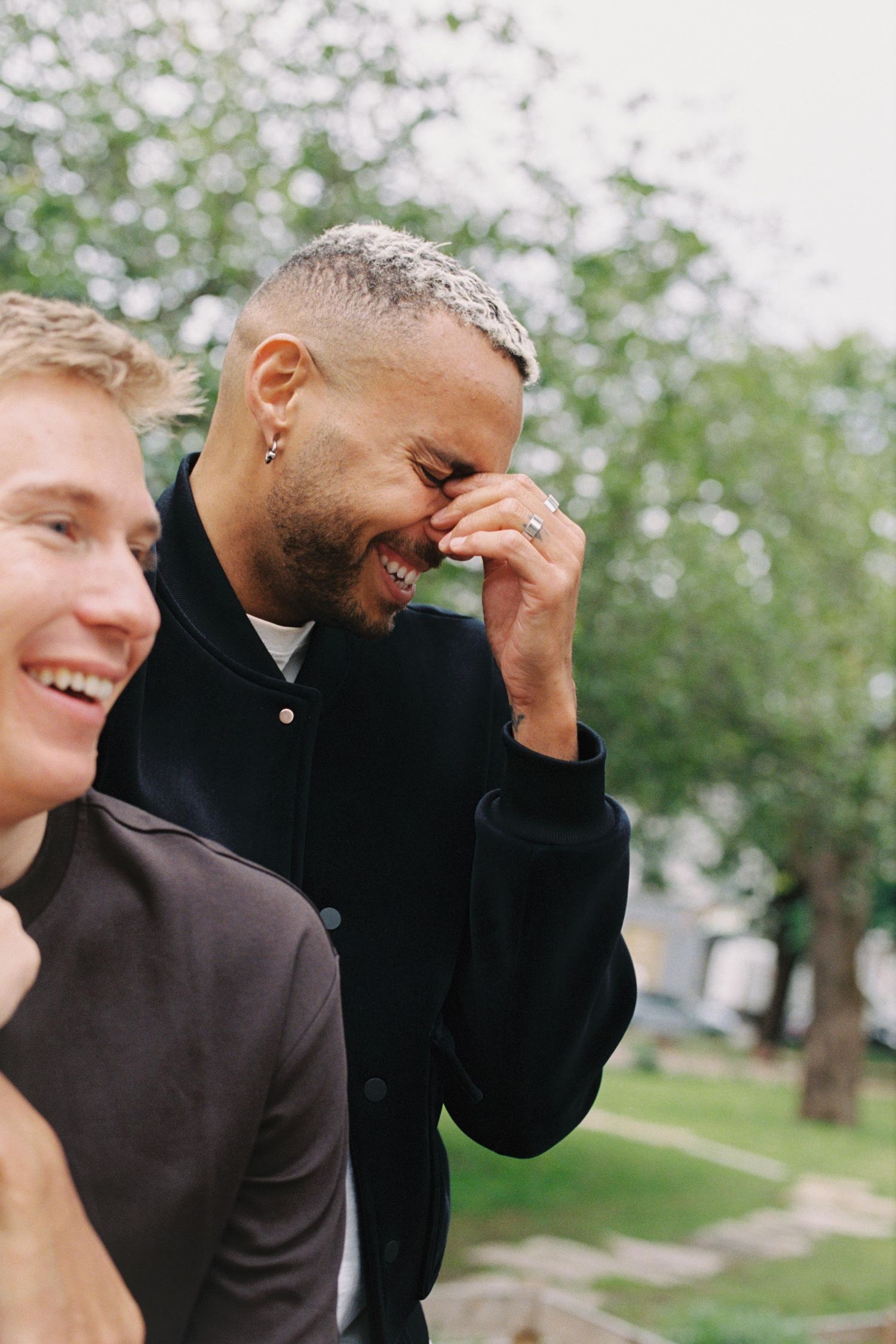 Two people laughing together outdoors on a sunny day with trees in the background.