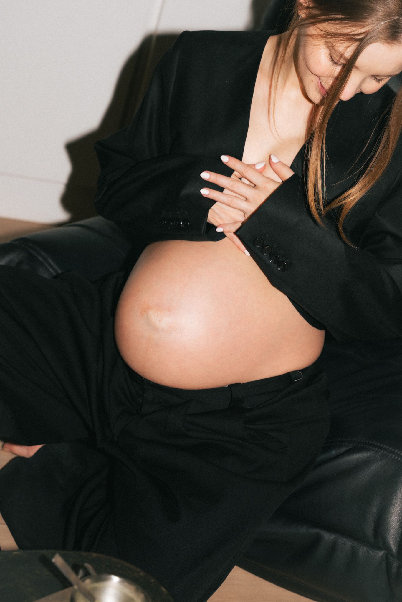 Close-up of an exposed pregnant belly with hands resting on it, wearing black clothing.