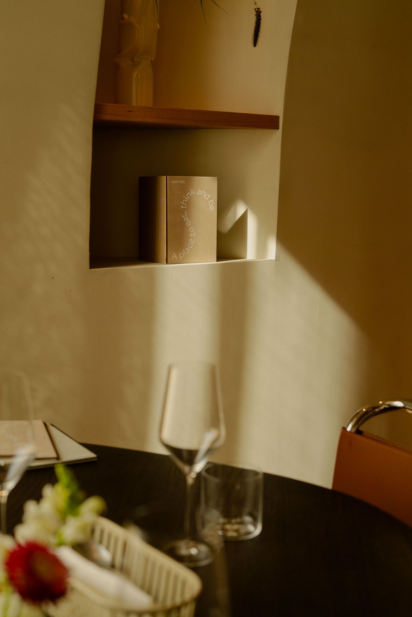 Minimalist dining setup with wine glasses and sunlight casting shadows on cream walls. Café Platz in Oslo.