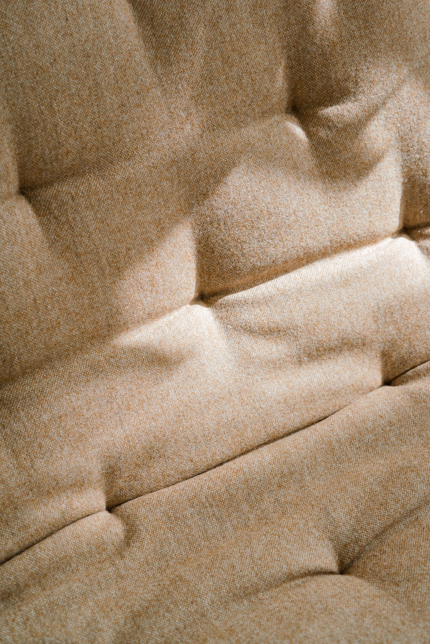 Close-up view of beige tufted upholstery texture with soft folds and button indentations.