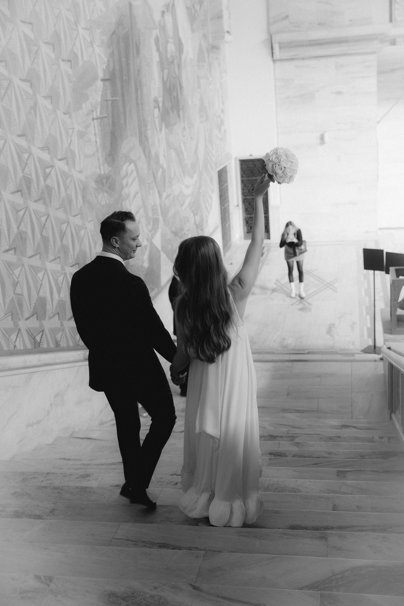A black and white photo series shows a couple walking together in a modern white interior space with geometric wall patterns.
