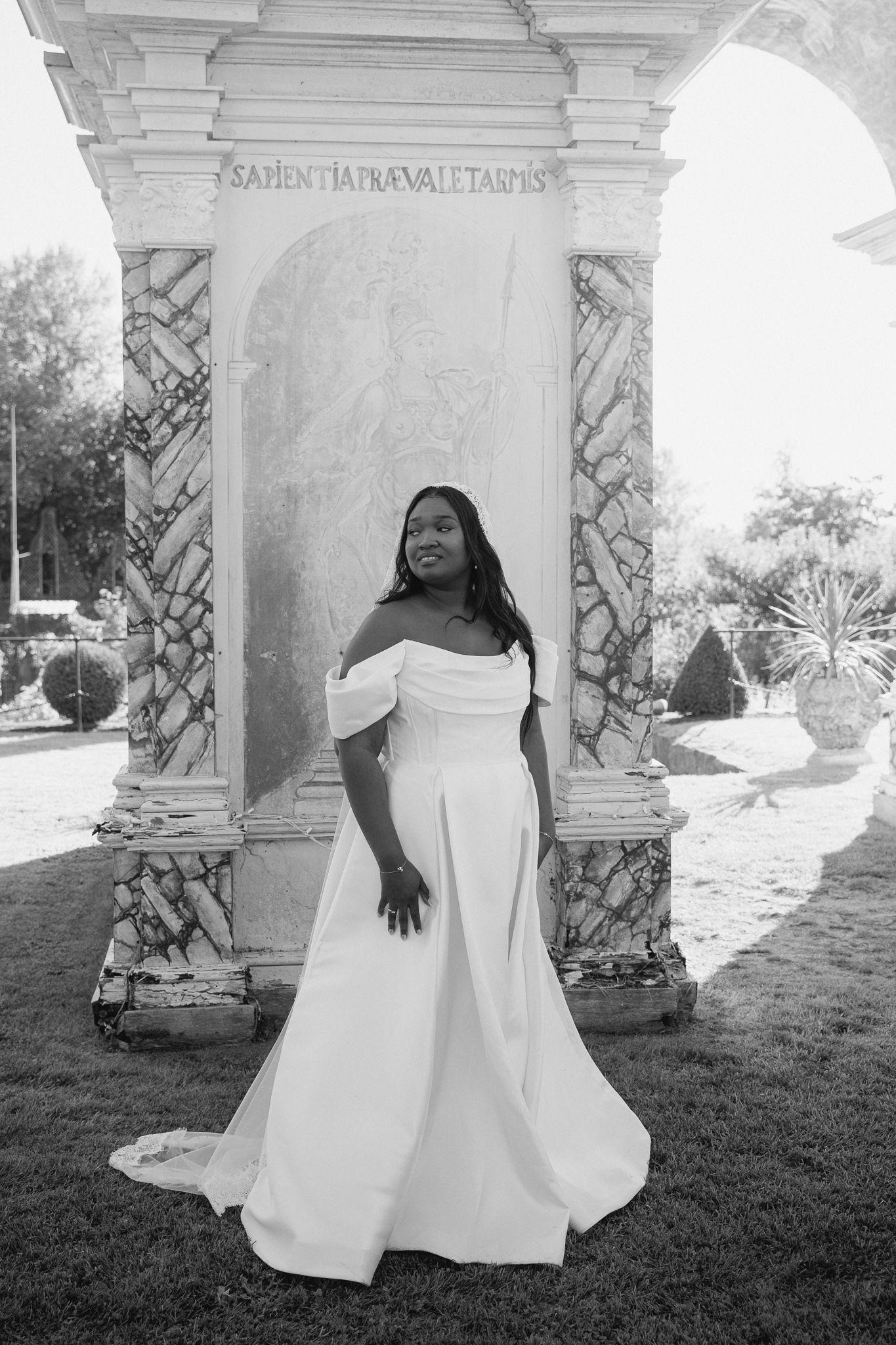 A black and white photo series showing someone in a flowing white dress sitting against a stone architectural column.