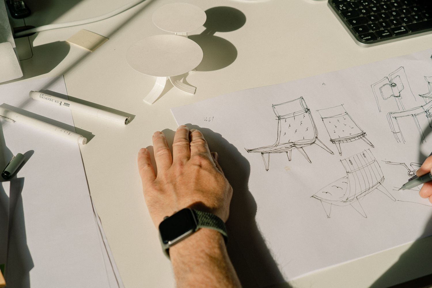 Hand sketching and drawing multiple design concepts on white paper with pencil.