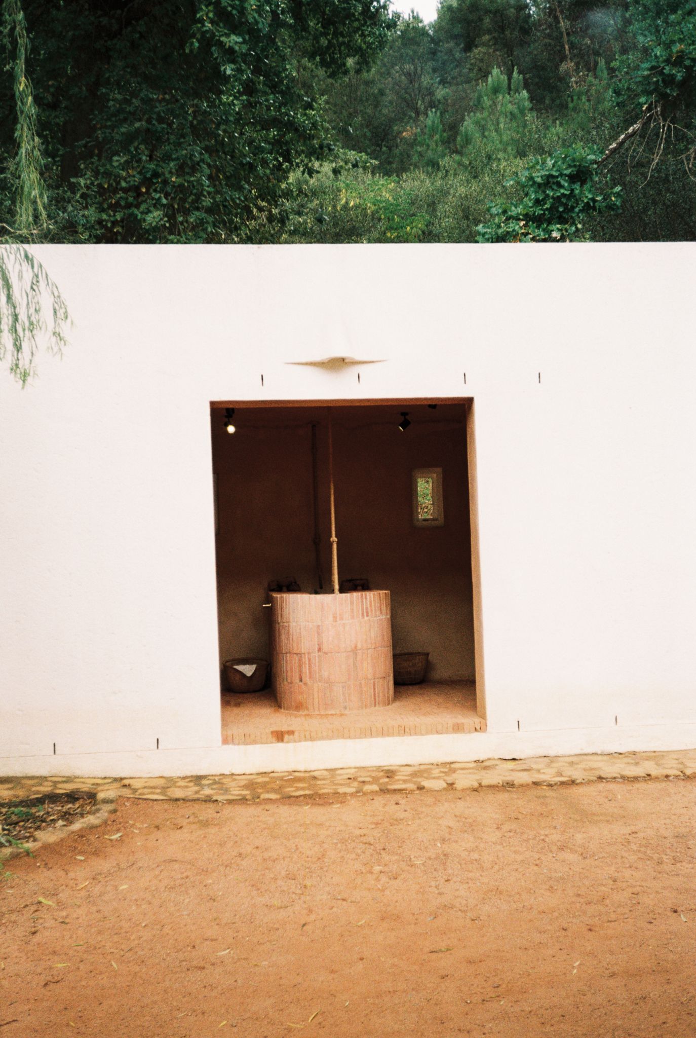 White stucco wall with open doorway revealing a traditional wooden barrel press inside a rustic winery building.