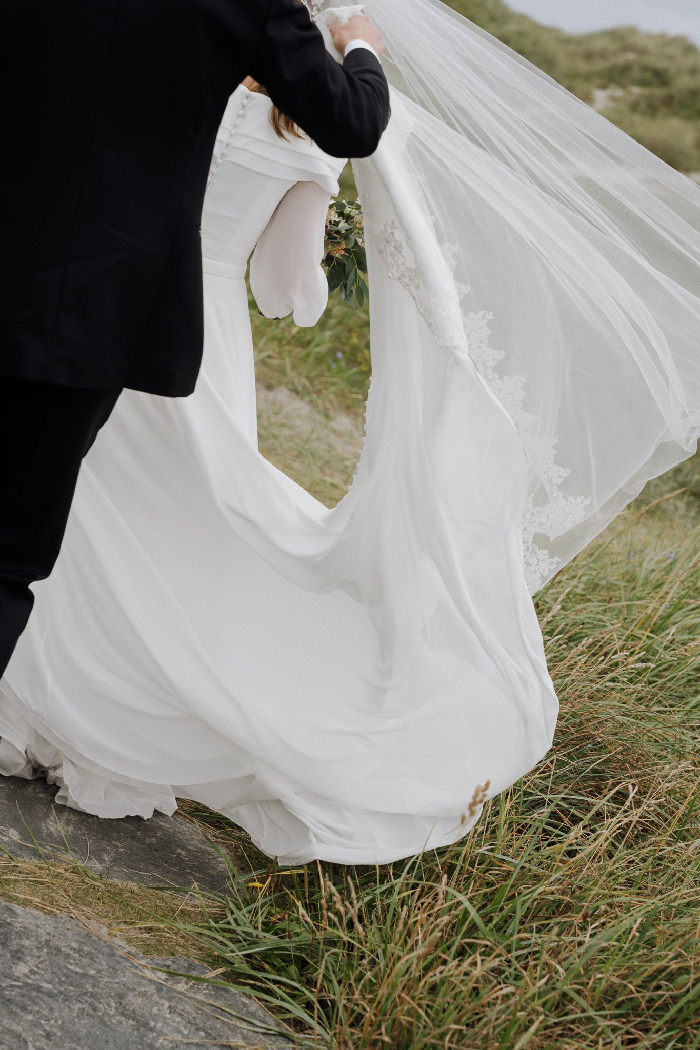 Flowing white wedding dress fabric billows gracefully in the wind against natural grass and stone background.