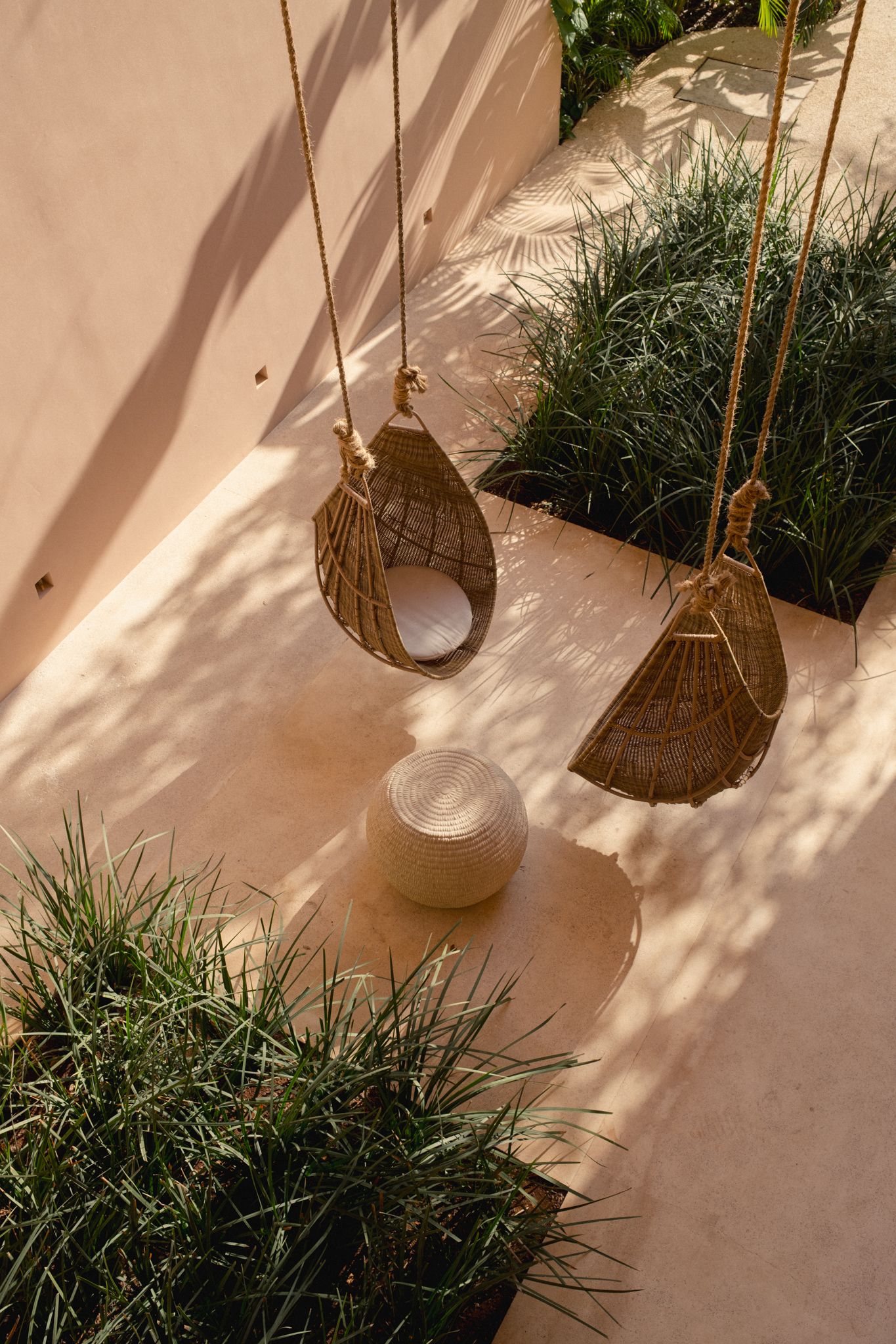 Hanging woven baskets and potted plants create a bohemian garden display against a sun-dappled wall at Aflora Tulum in Mexico.