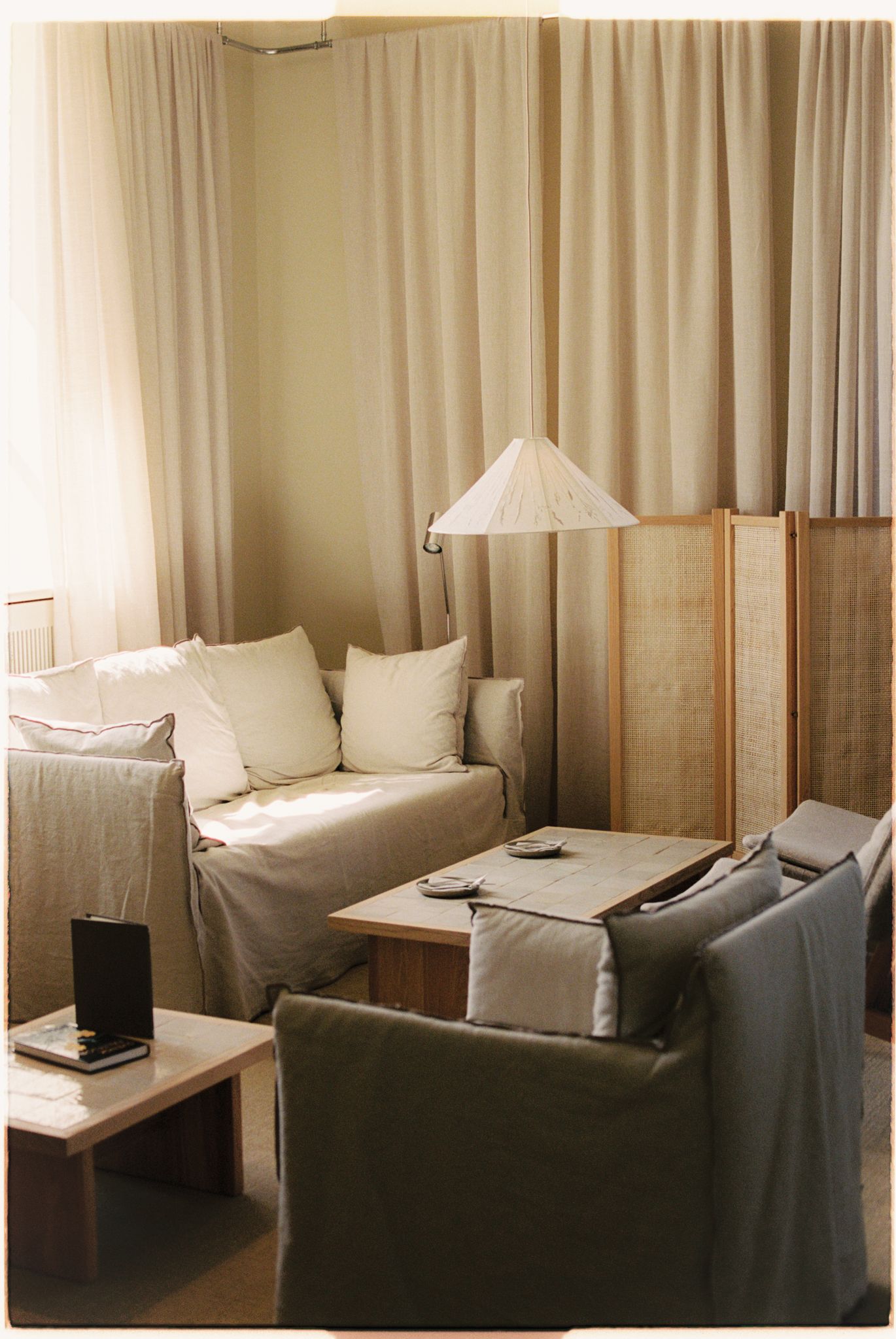 Minimalist living room with neutral linen sofa, wooden coffee table, floor lamp, and sheer curtains in soft beige tones.