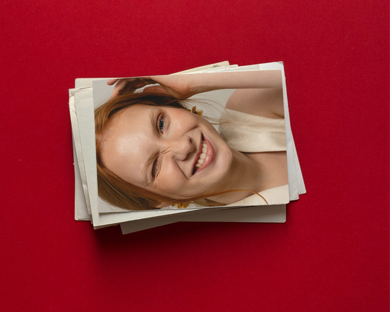 Stack of printed photos on red background featuring a smiling young woman with blonde hair in a white top.