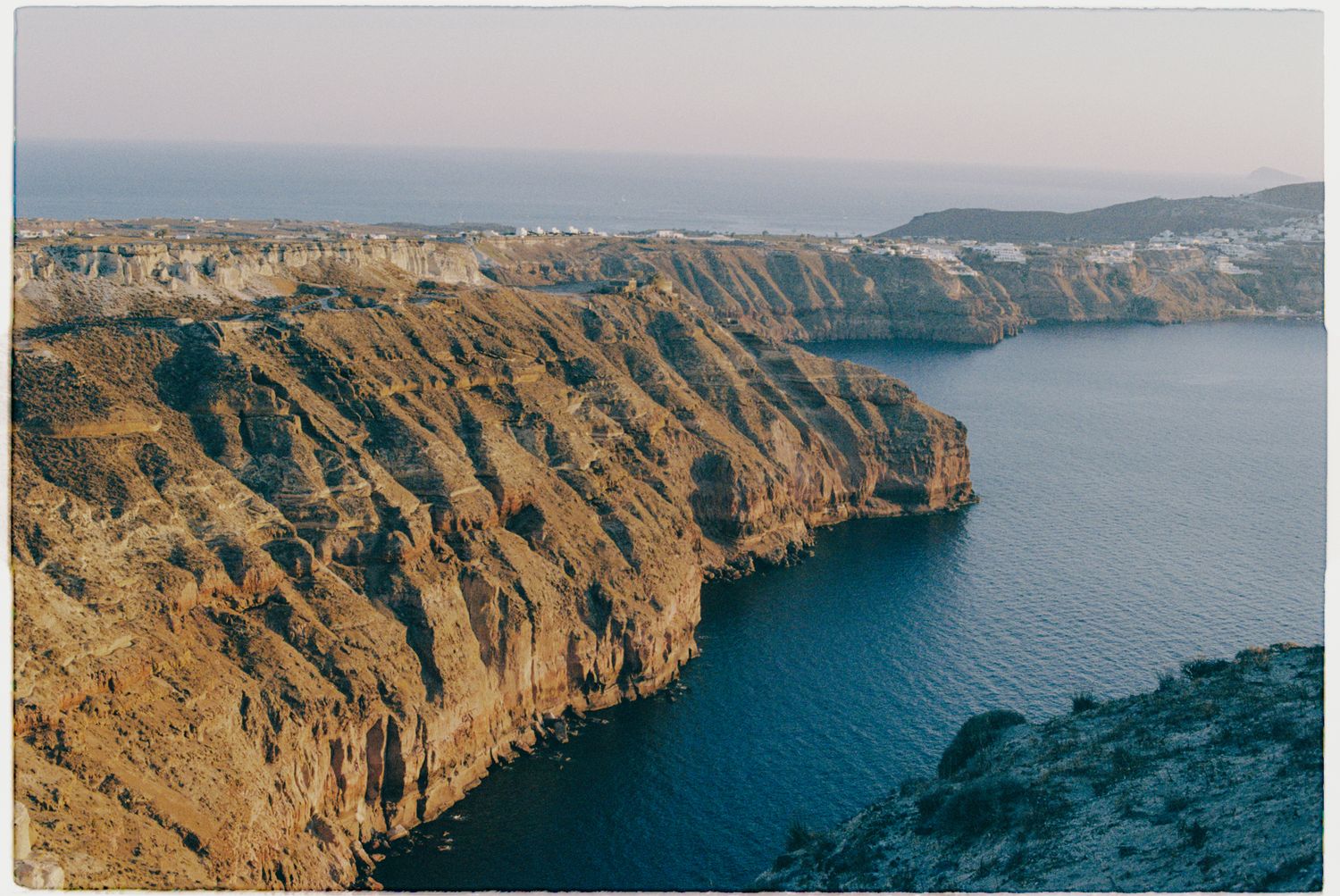 Panoramic aerial view of rugged coastal cliffs overlooking deep blue Mediterranean waters at sunset.