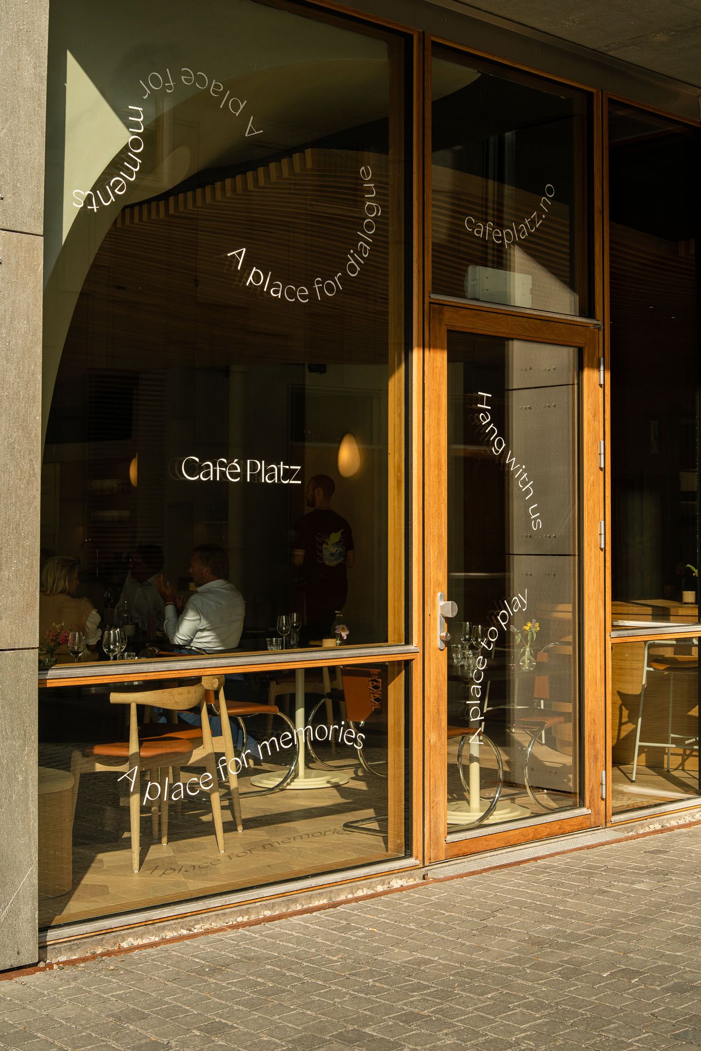 Modern cafe storefront with large windows and wooden frames displaying 'Cafe Platz' signage.