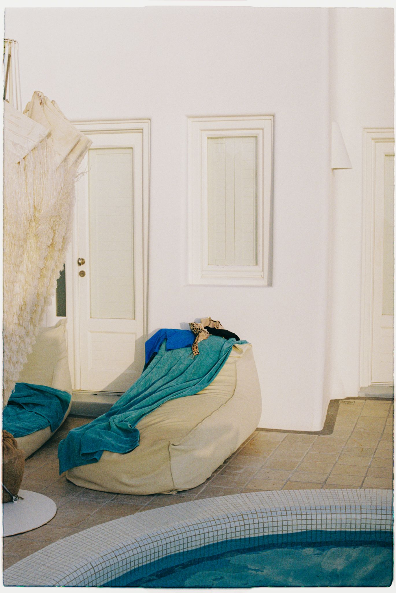 A beige lounge chair with turquoise fabric sits beside an indoor pool with white walls and tiled flooring.