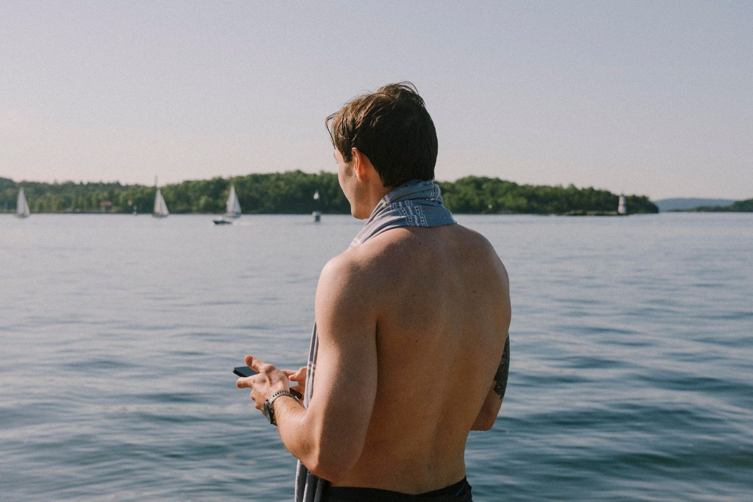 A person fishes from a boat on calm blue waters surrounded by distant shoreline on a sunny summer day.
