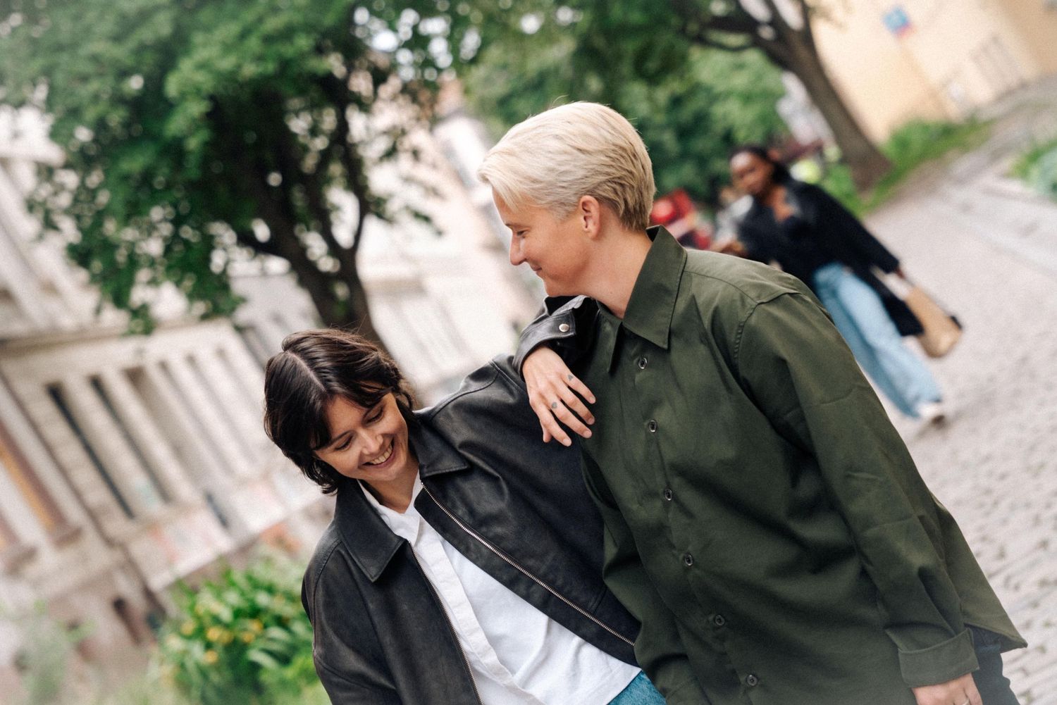 Two people share a candid moment while walking together outdoors on a path with greenery in the background.