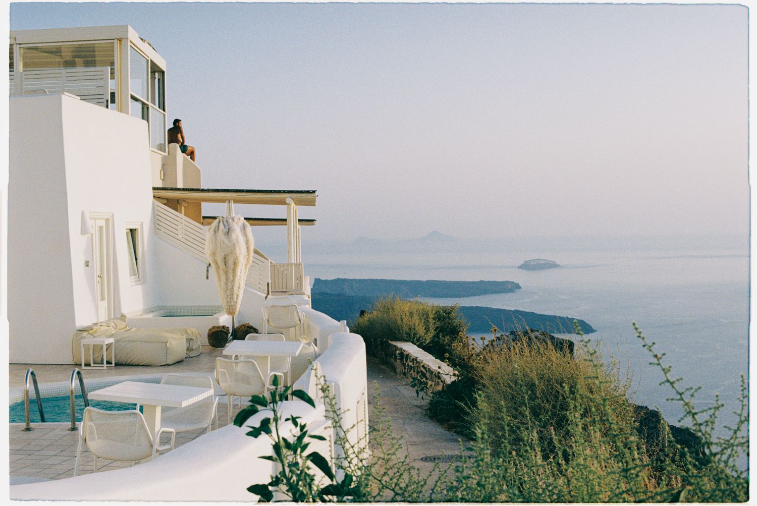 Whitewashed Mediterranean villa terrace overlooking a serene blue sea with distant islands on the horizon.