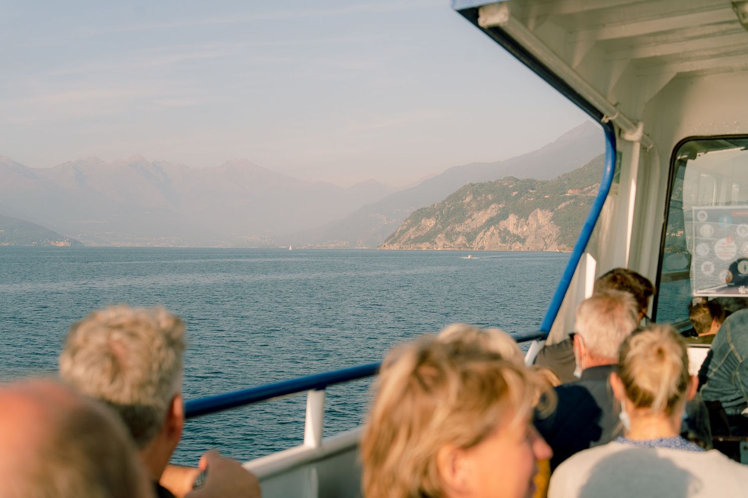 Passengers on a boat cruise looking out at scenic mountain coastline views on a sunny day in Lake Como, Italy.