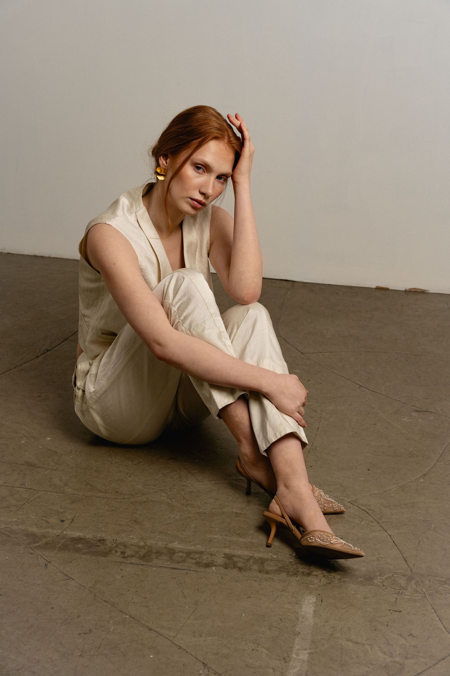 A person in white clothing sits curled up on a gray concrete floor in a minimalist artistic photo series.