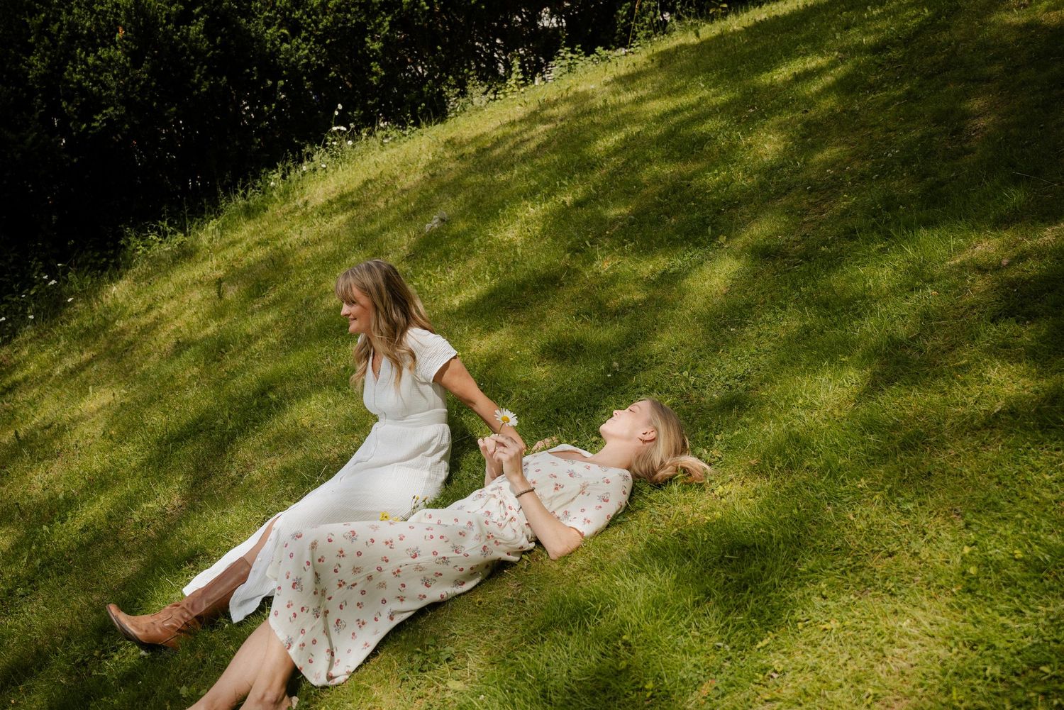 A person in a floral dress lies on a grassy hillside while enjoying a sunny summer day.