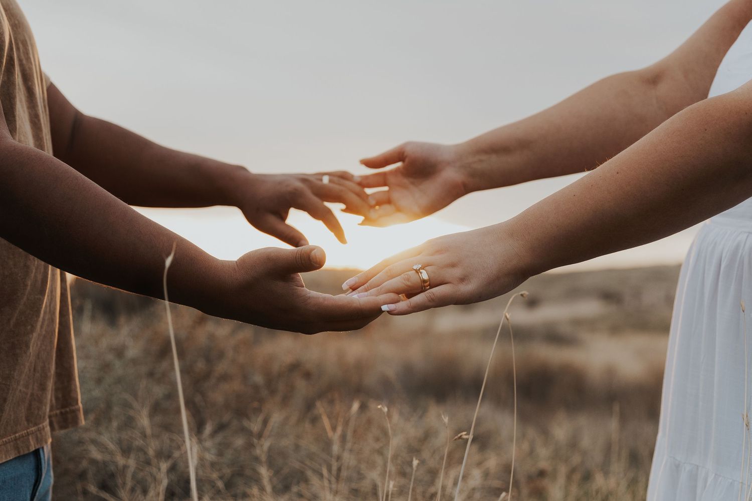 Gentle hands reaching towards each other in warm sunlight against a blurred natural backdrop.