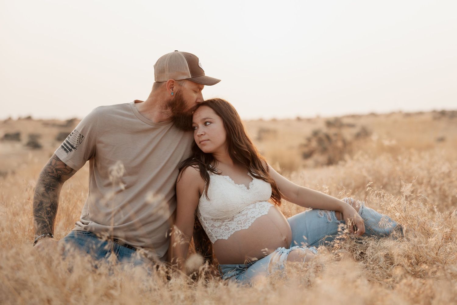 Couple relaxing together in golden field during maternity photoshoot.