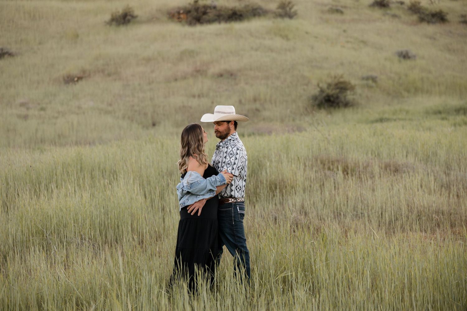 Romantic couple embracing in tall grass field at golden hour.