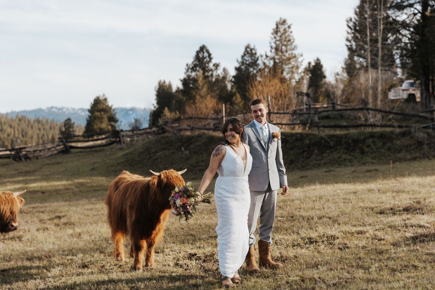 A couple poses with a Highland cow in a scenic mountain pasture setting.