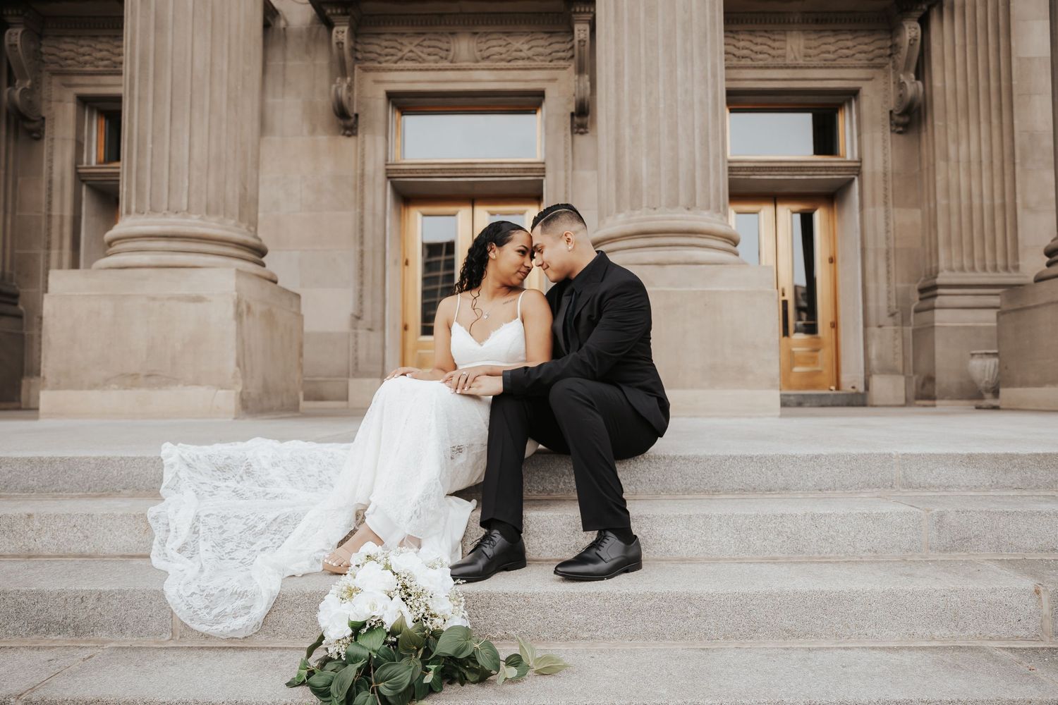 Wedding couple shares intimate moment on grand stone steps with floral decor.