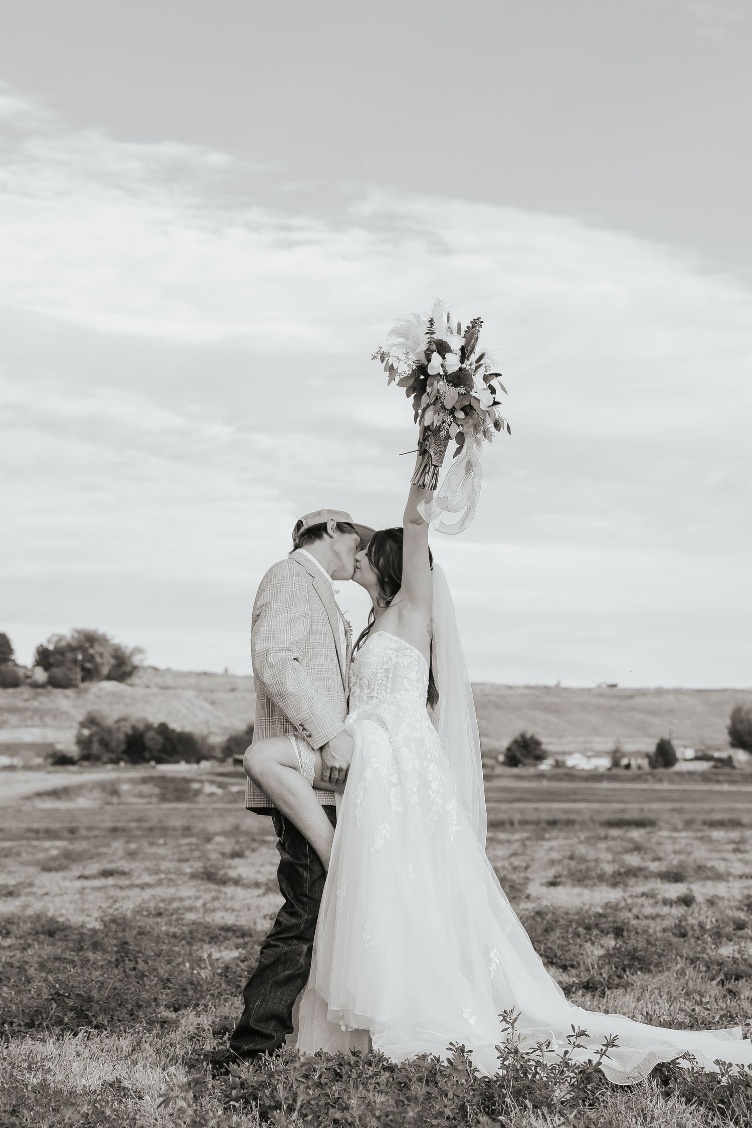 A romantic black and white wedding photo of a couple embracing in a scenic field.