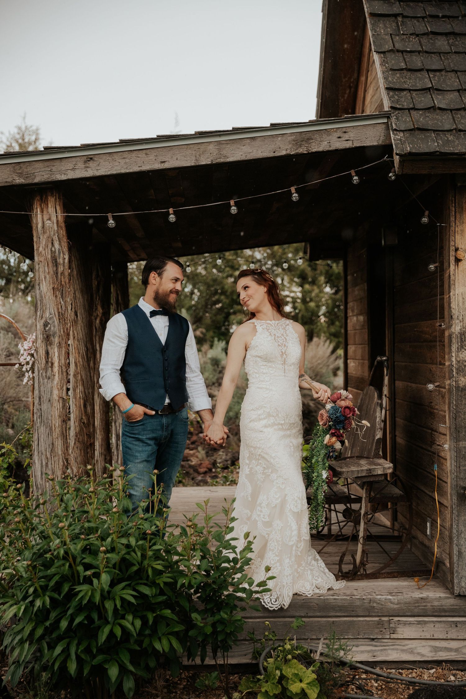 Rustic wedding portrait at wooden cabin entrance with string lights.