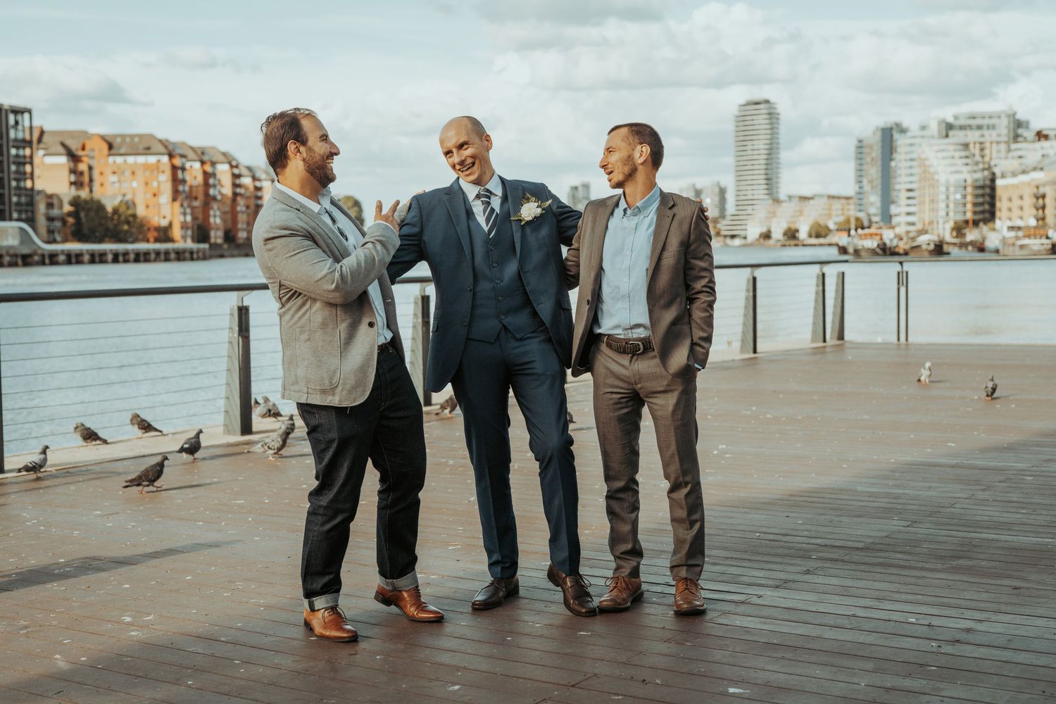 A group of people gather on a wooden pier overlooking Boston Harbor and city skyline.