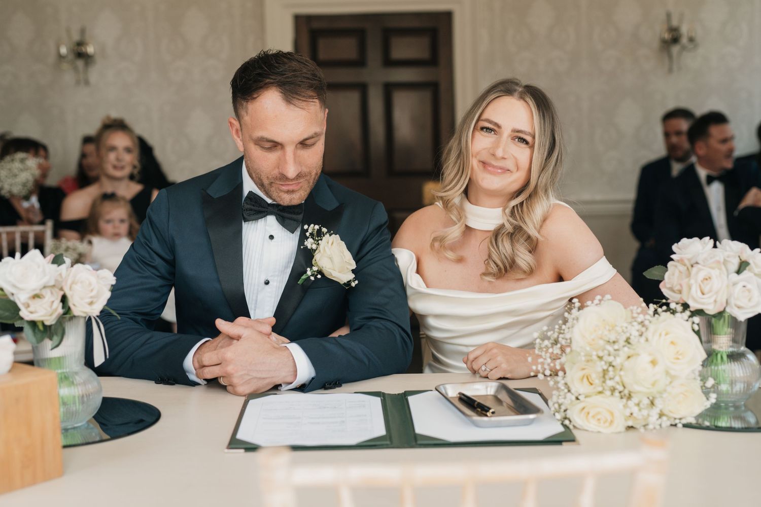 Couple sitting at elegant wedding reception table with white floral centerpieces and formal place settings.