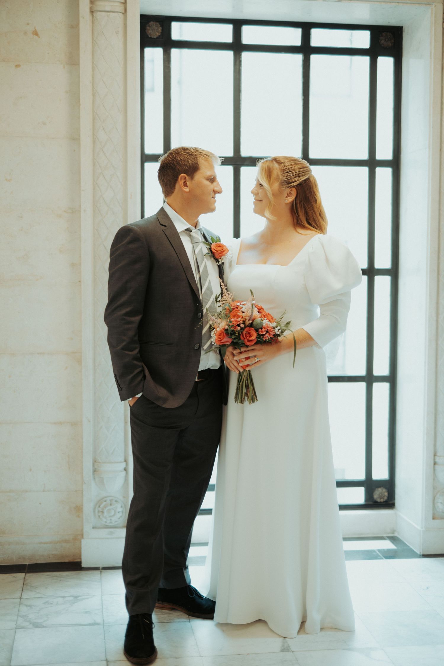 Elegant wedding couple shares intimate moments in a bright minimalist room with large windows.