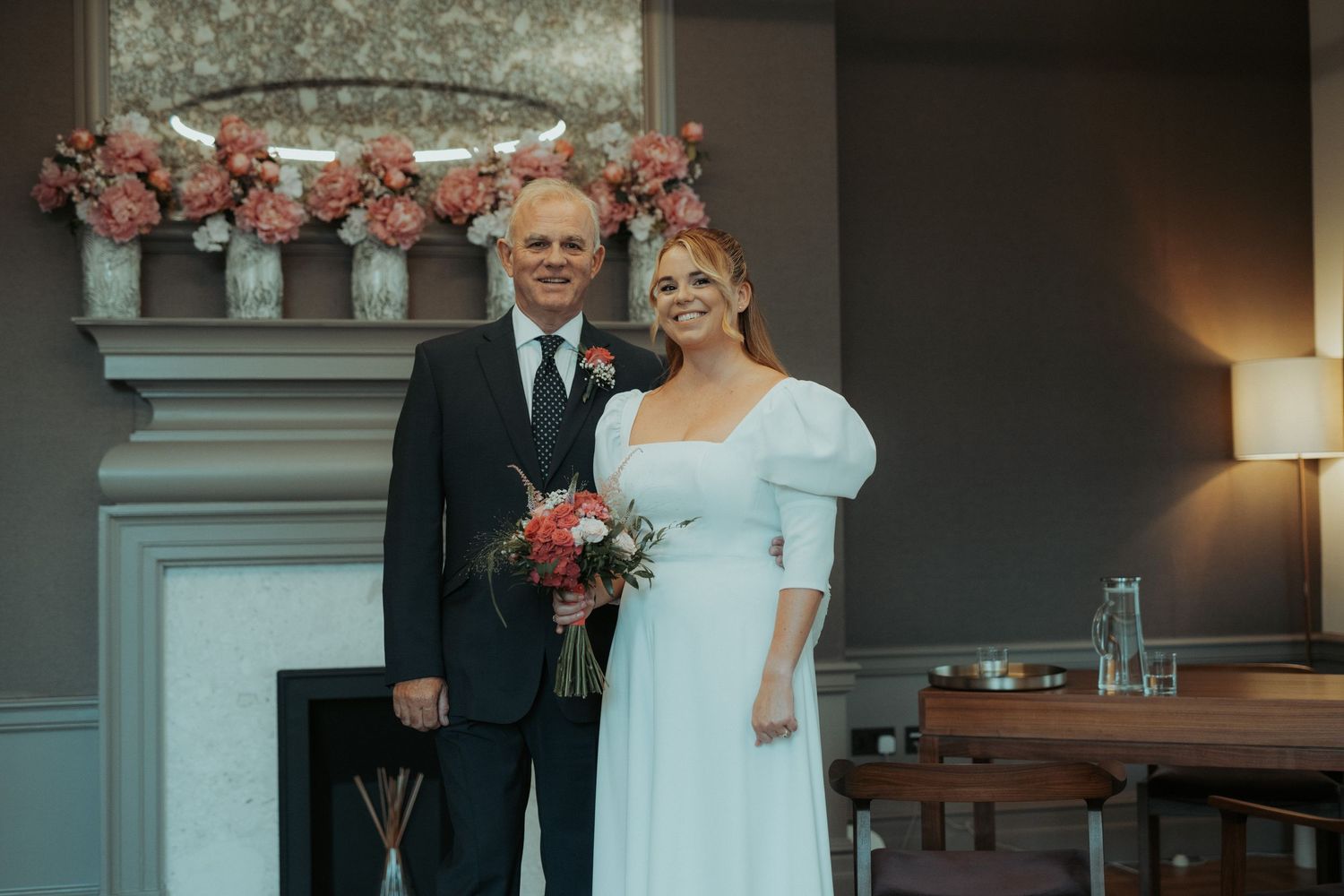 A couple poses together in formal wedding attire in front of a white church building.