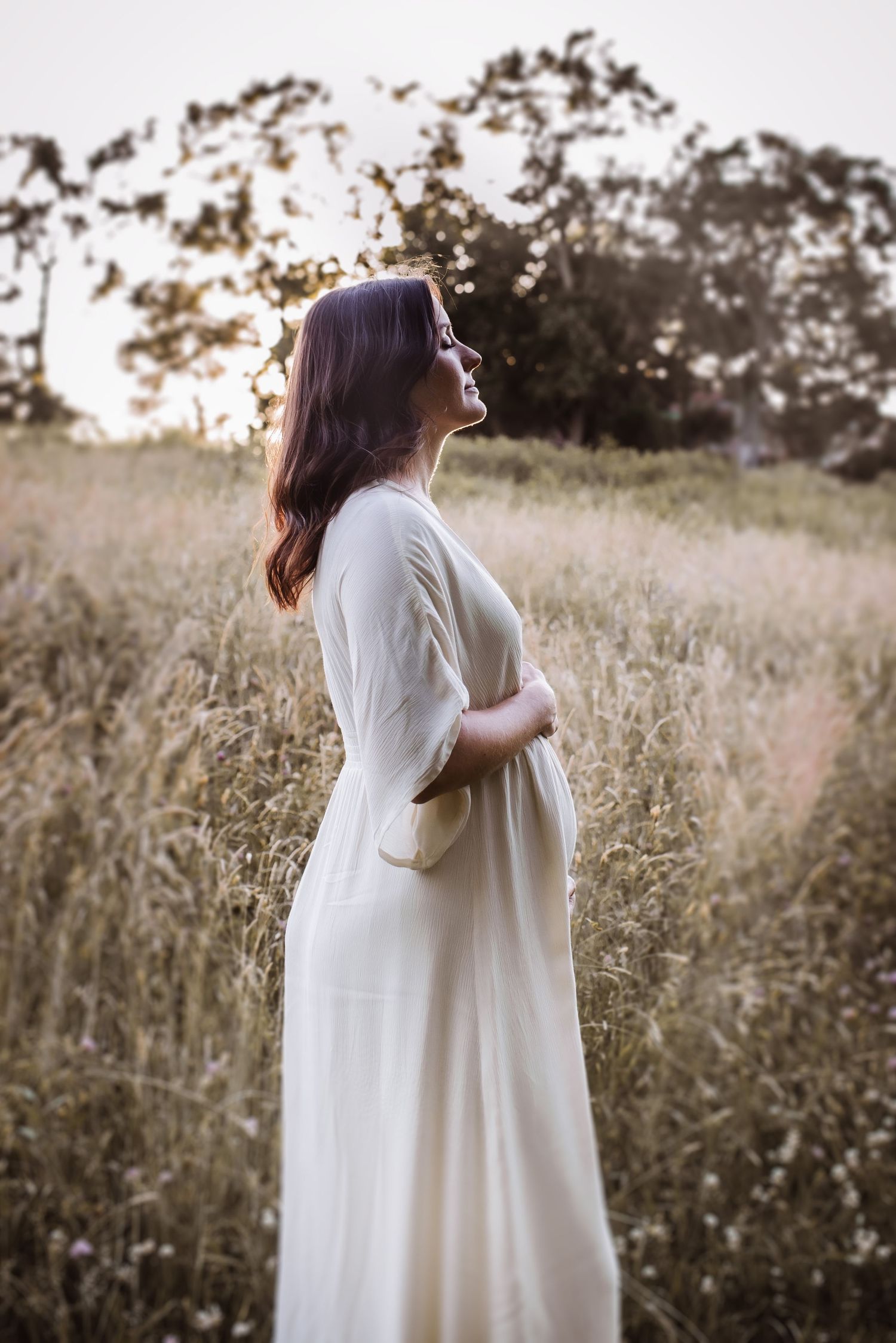 Person in flowing white dress poses gracefully in a golden field at sunset.