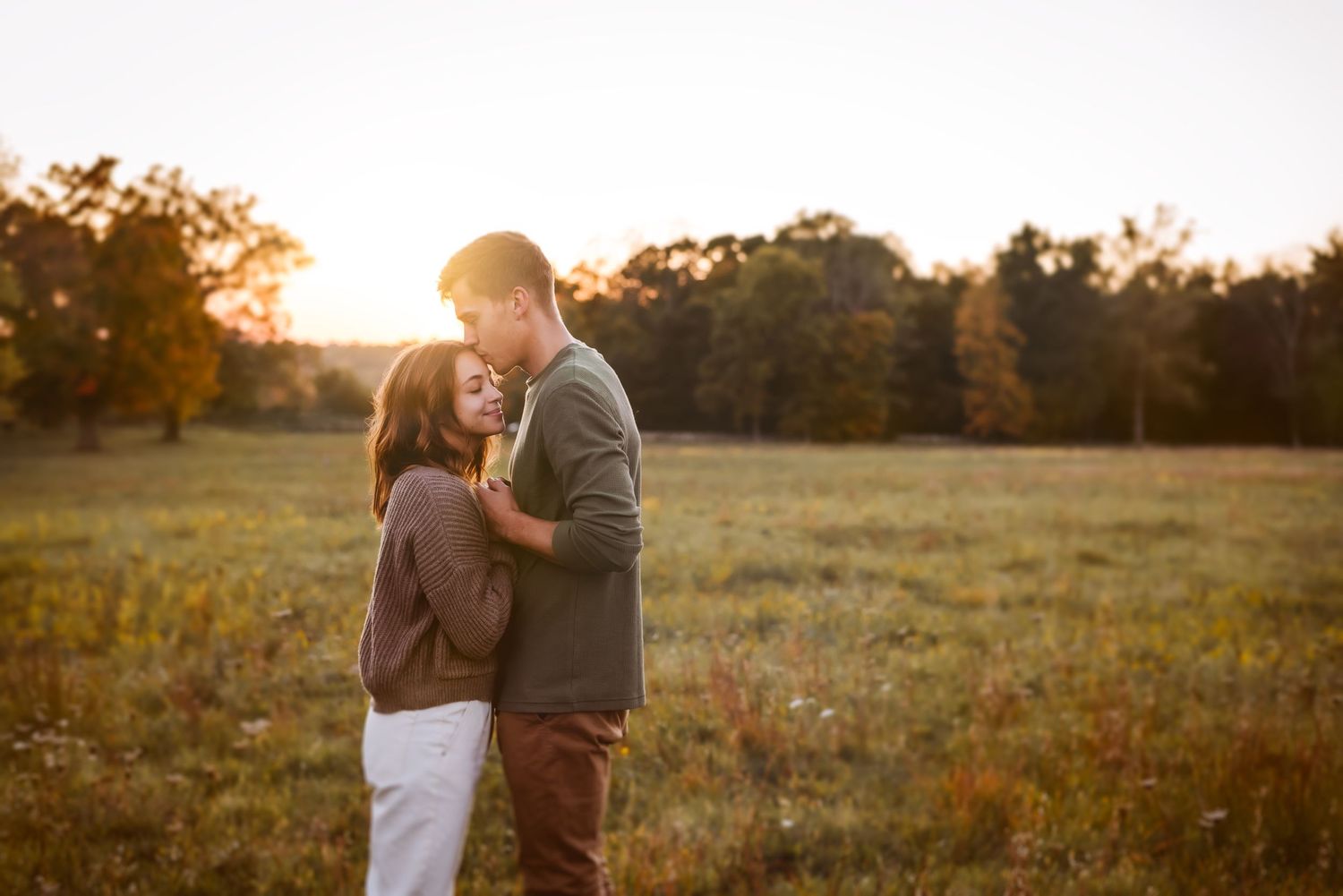 Couple sharing tender moment in golden field during sunset.