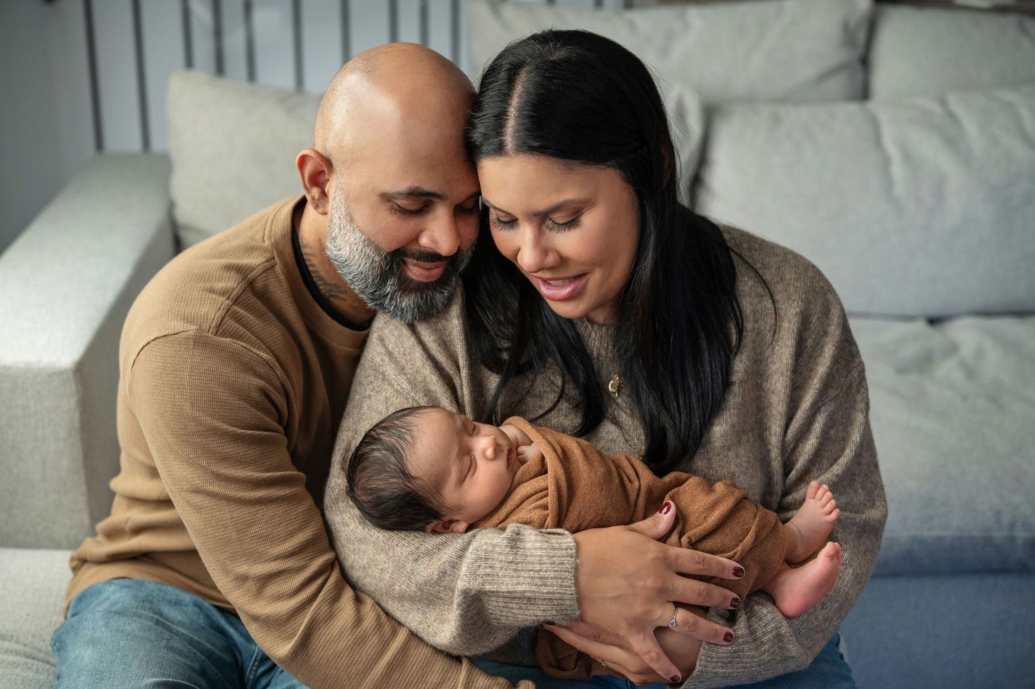Parents sharing intimate moments with their newborn on a grey couch.