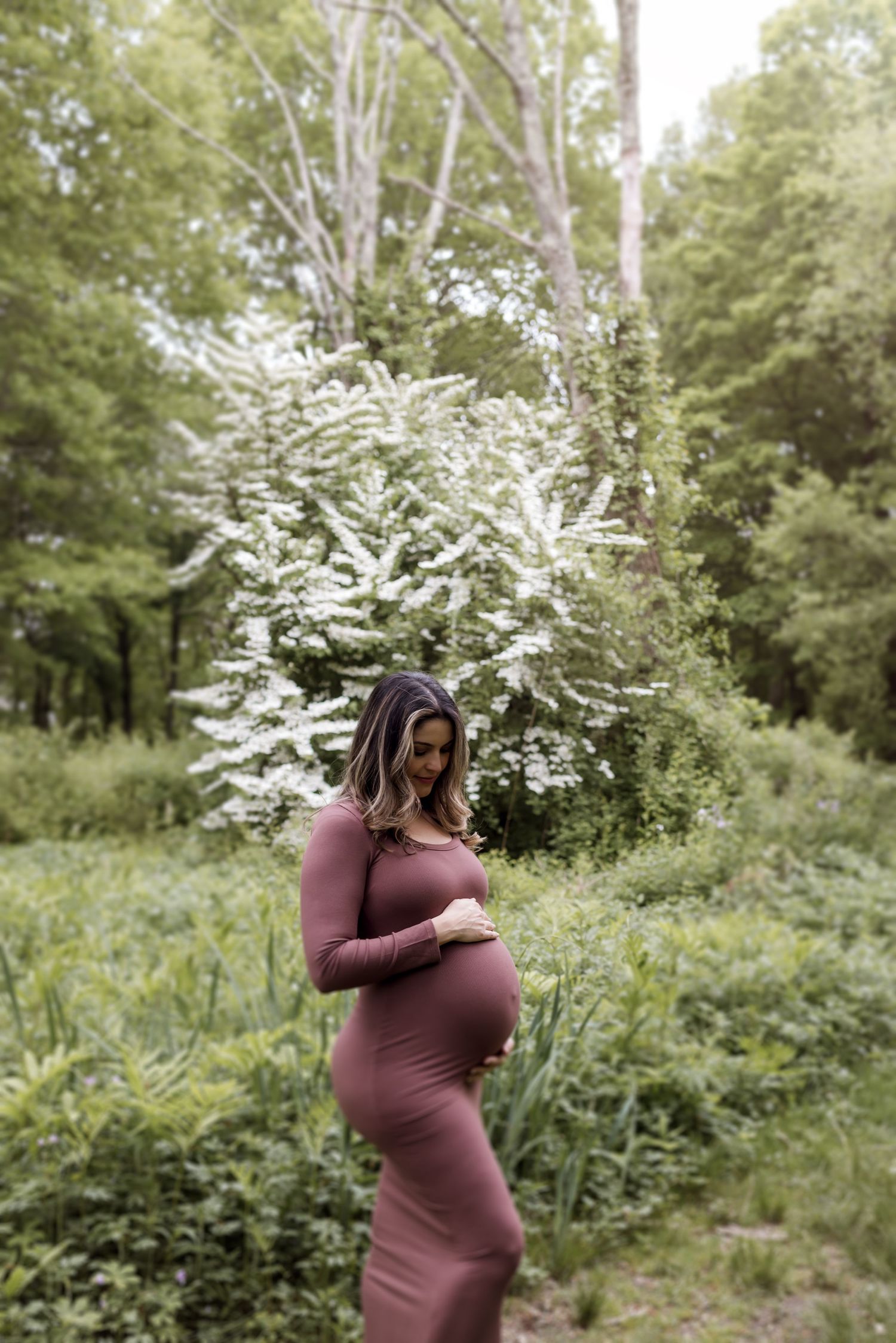 A maternity photo shoot in a natural setting with flowering trees and greenery.