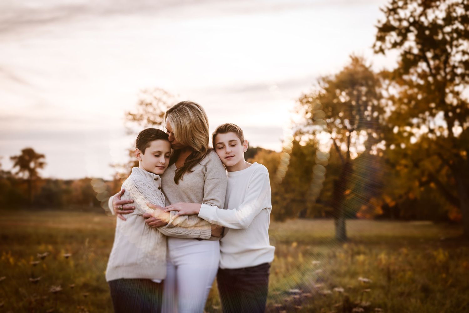 A couple shares a romantic embrace during golden hour in a rustic outdoor setting with autumn trees in the background.