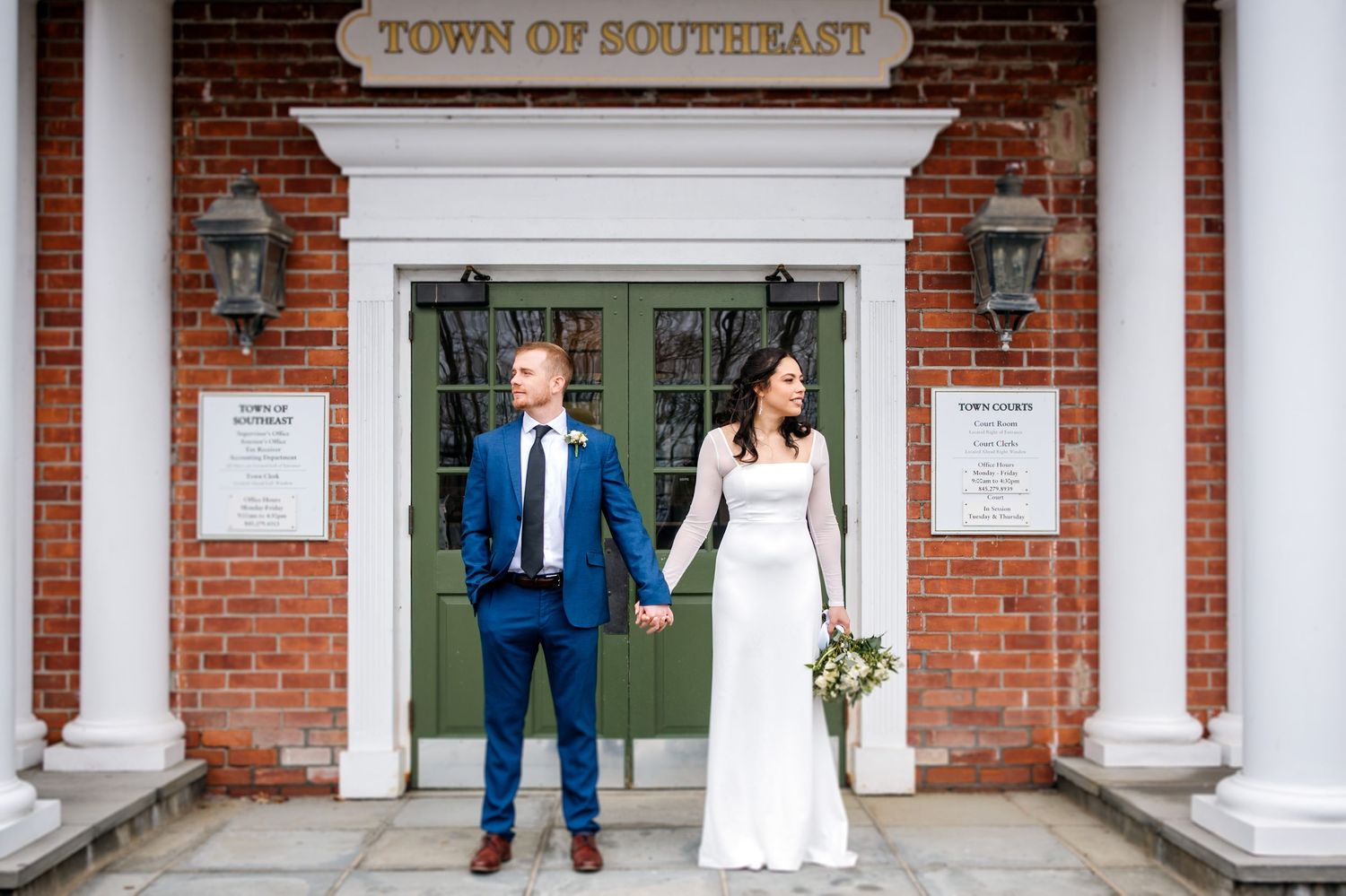 Wedding couple standing in front of a brick building with white columns and 'Town of Southeast' signage.