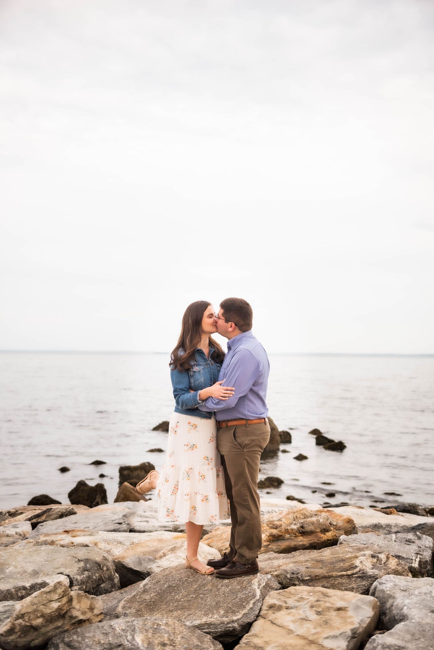 Romantic couple sharing intimate moments on rocky beach during seaside photoshoot.