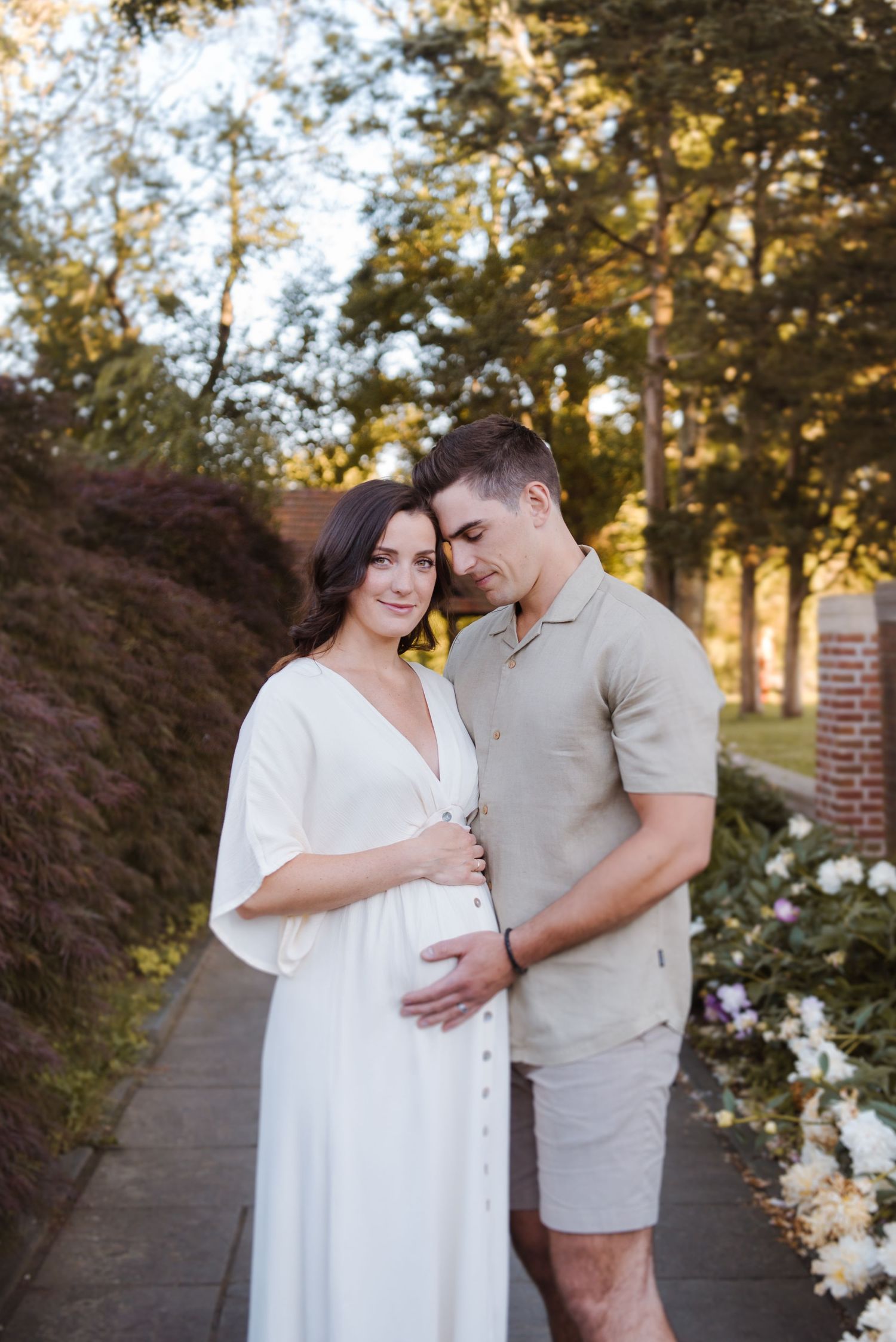 A couple embraces tenderly in an outdoor setting with golden sunlight filtering through trees.