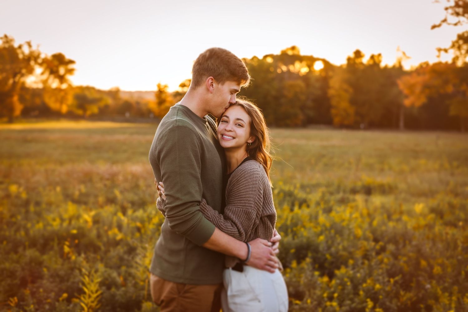 Couple embracing in sunlit field during golden hour photo session.