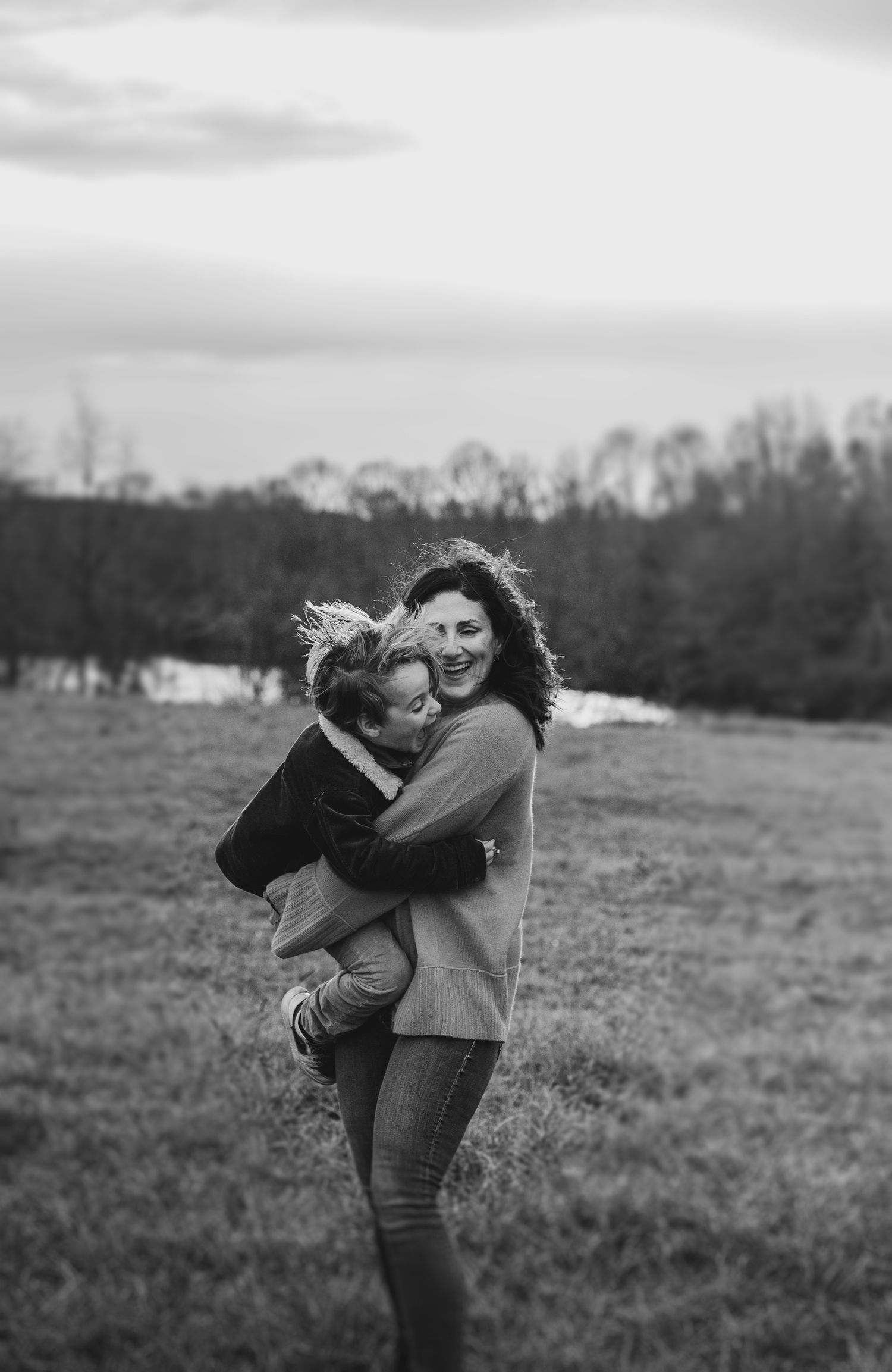Black and white portrait of playful moment in open field with trees in background.