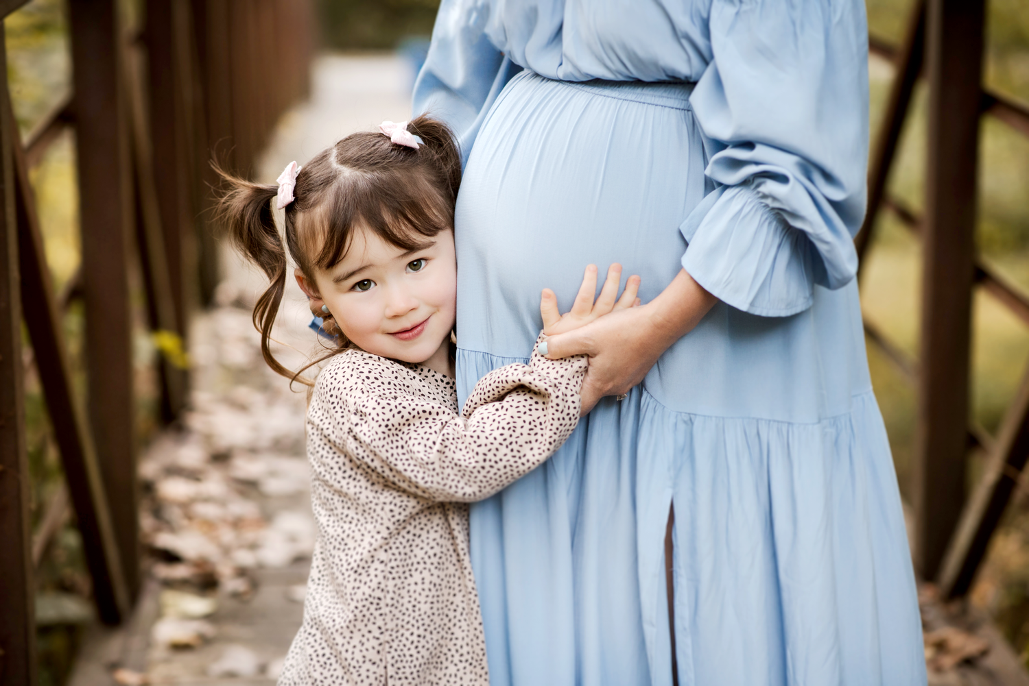 A tender family moment captured in soft lighting against a rustic wooden fence.