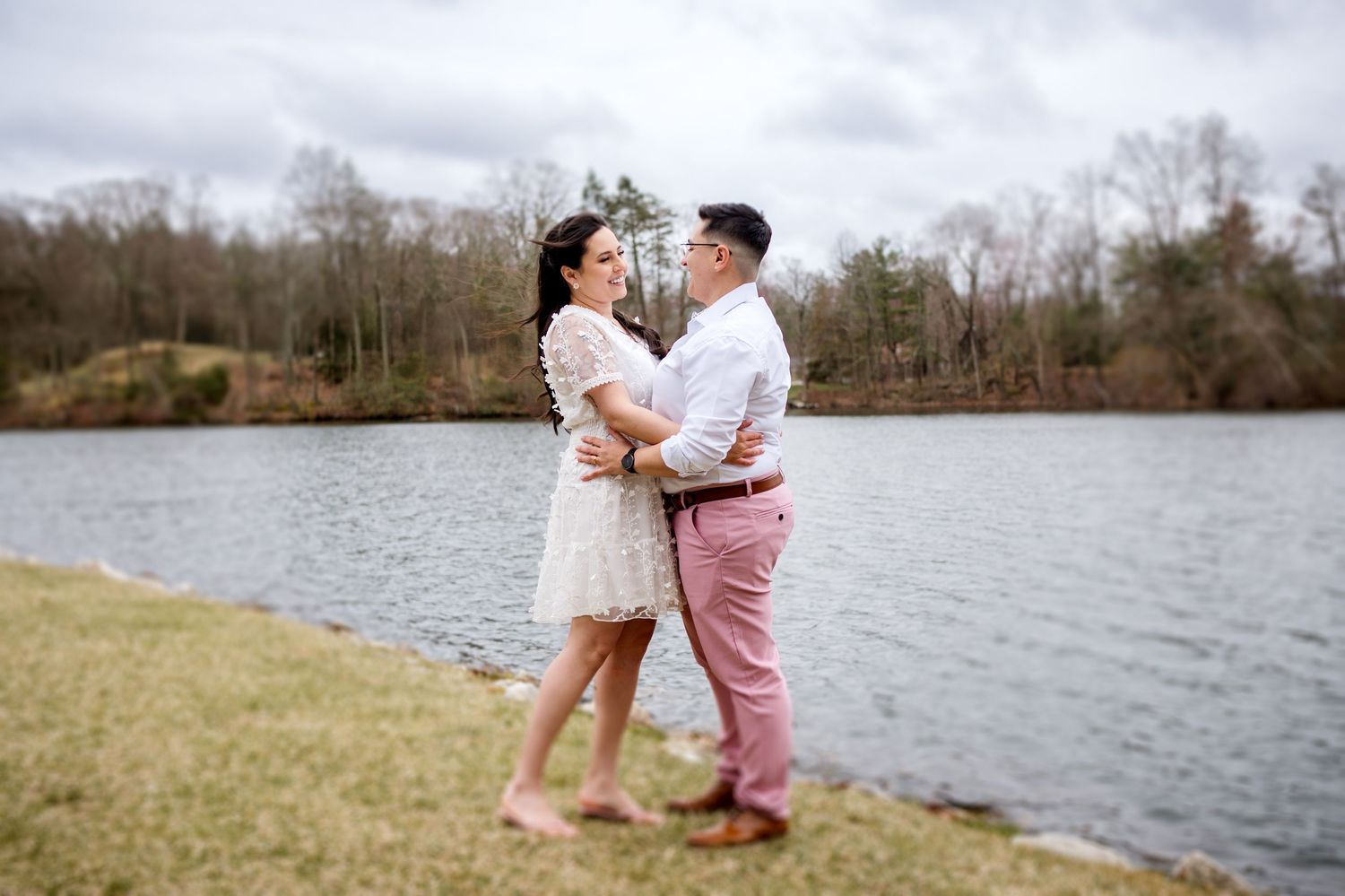 Wedding couple embracing by a serene lake on an overcast day.