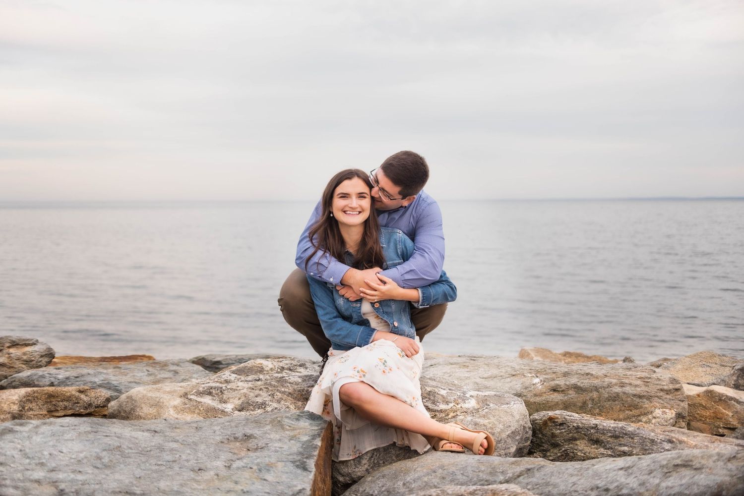 Couple embracing on coastal rocks with ocean waves in background.