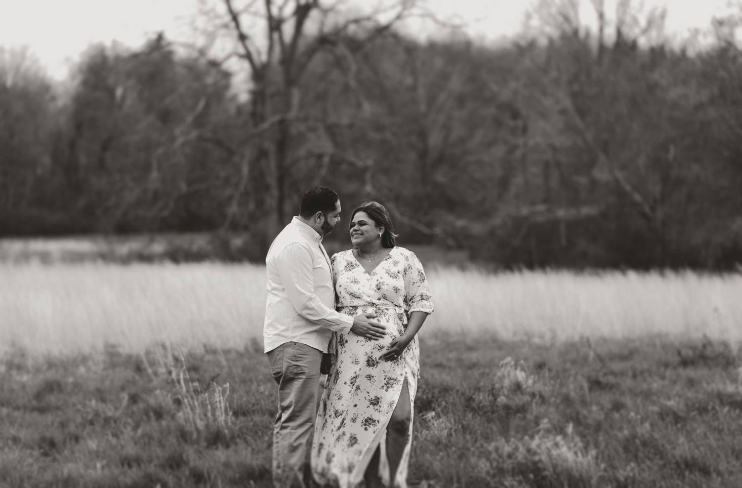 Couple walking together through a winter field with bare trees in the background.
