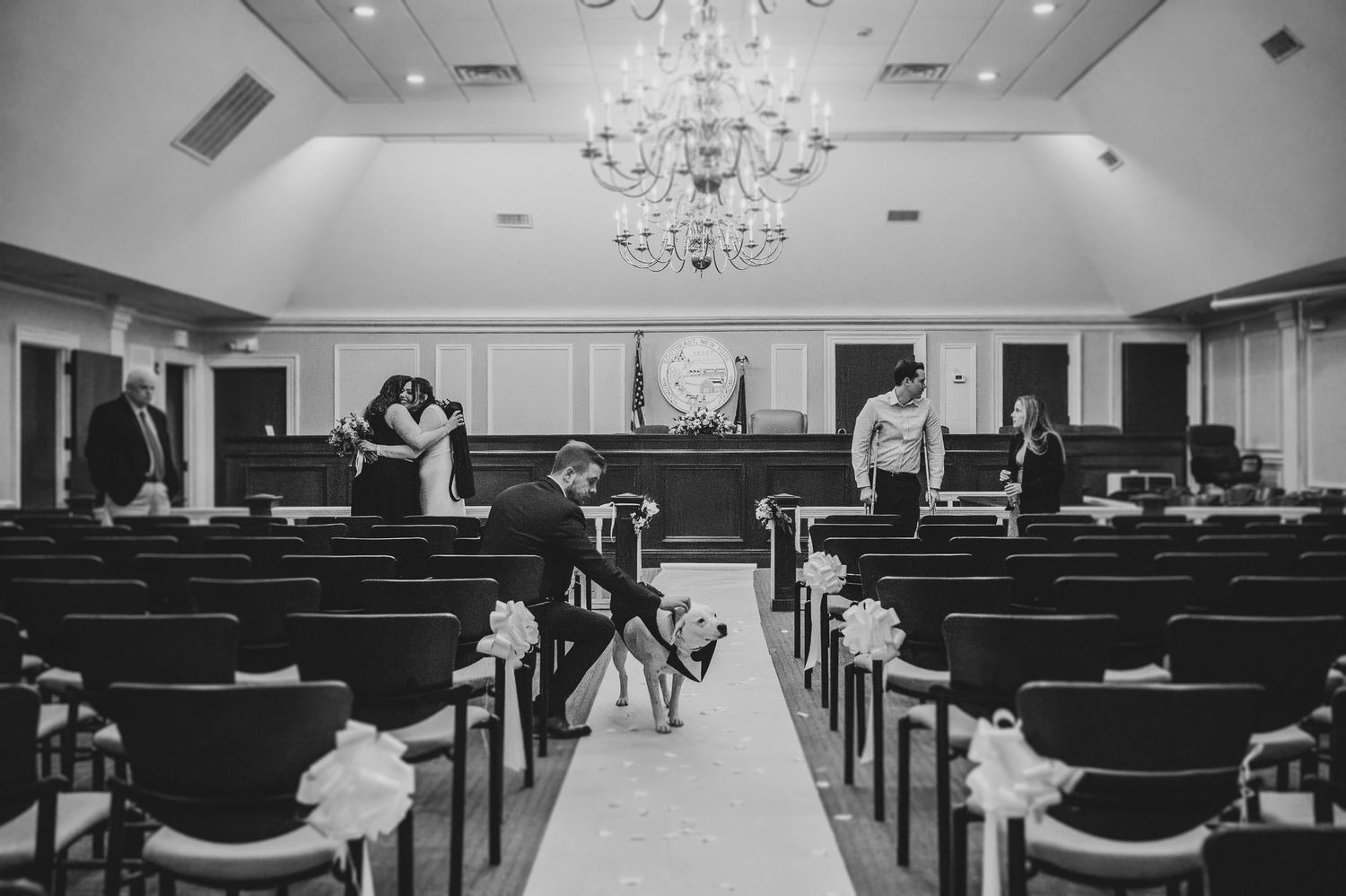 Black and white photo of a wedding ceremony venue with elegant chandeliers and rows of chairs.