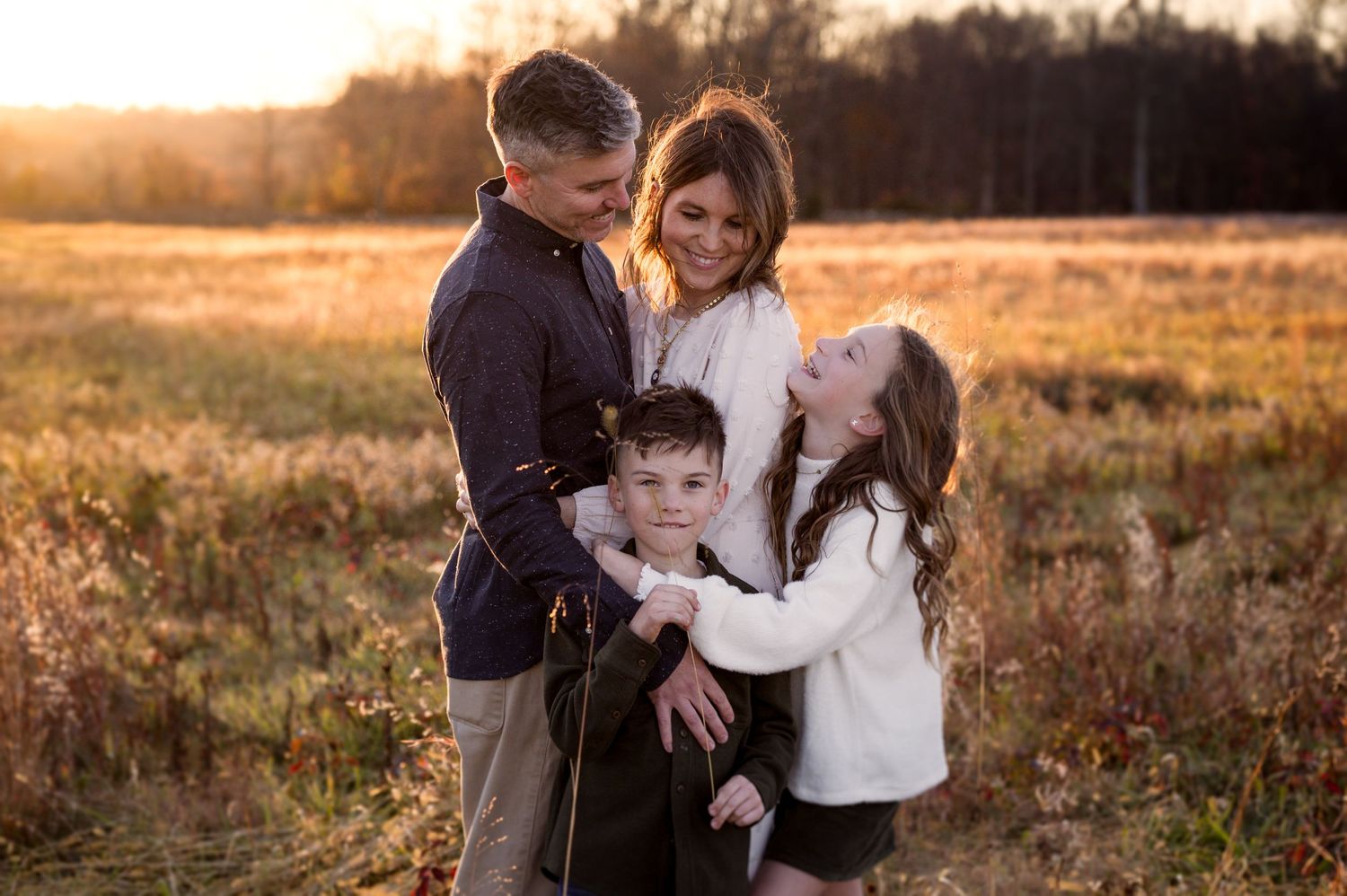 Family shares affectionate moments together in a sunlit autumn field.