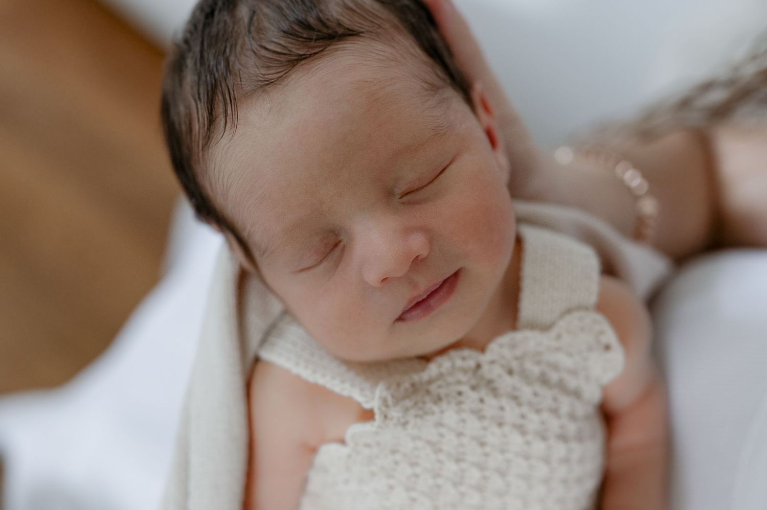 Sleeping newborn in delicate white lace outfit on soft bedding.